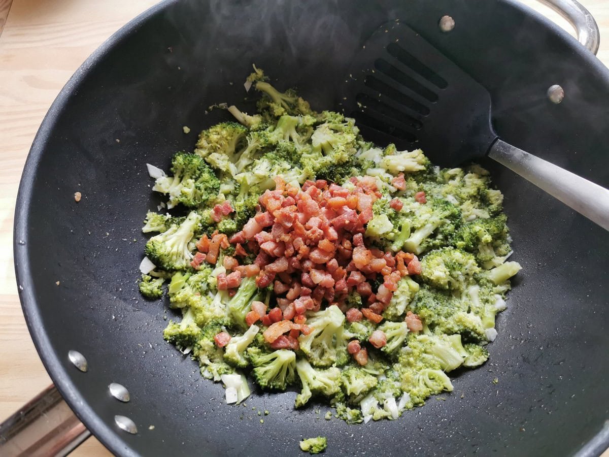 Cooked pancetta cubes in a frying pan with cooked broccoli florets.