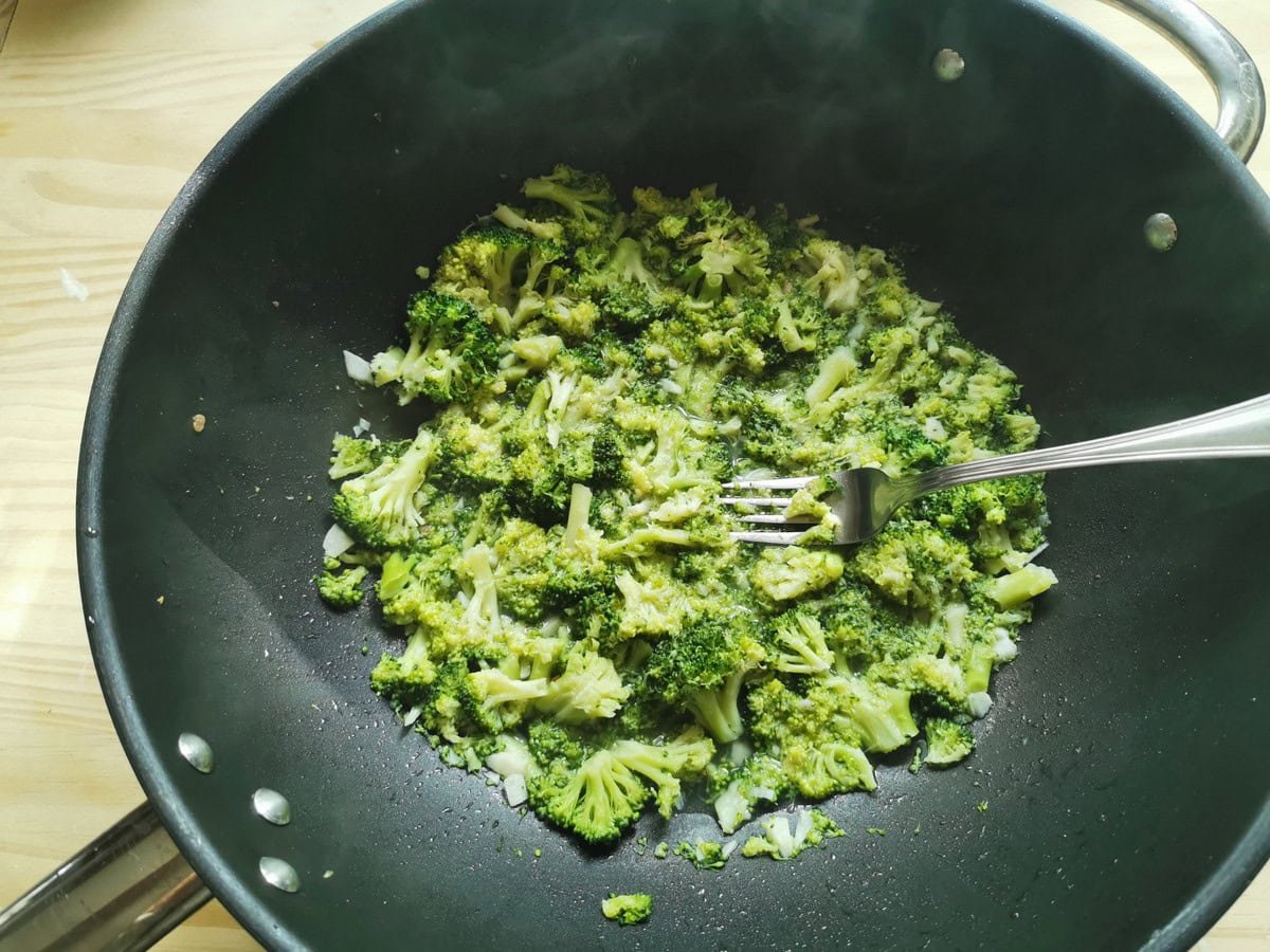 Broccoli florets in a pot with chopped garlic and a fork.