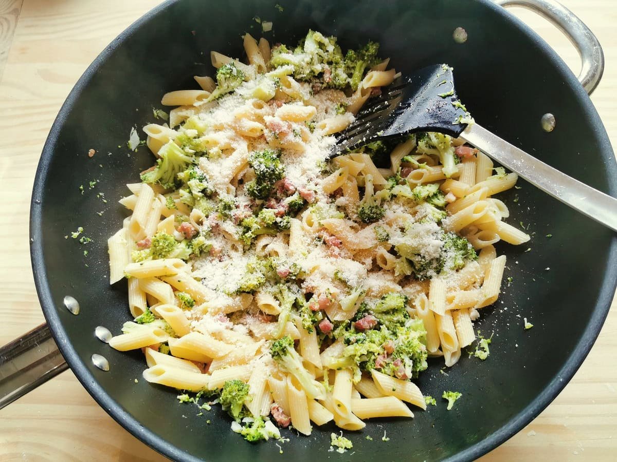 Grated grana cheese added to frying pan with pasta and broccoli.