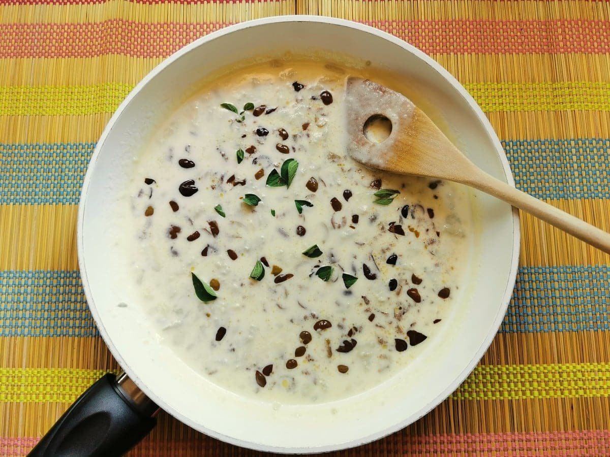 Fresh marjoram added to creamy gorgonzola and olive sauce in white pan for pasta alla cenere.