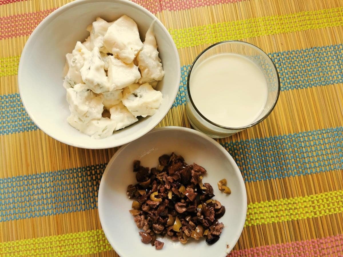 Ingredients for pasta alla cenere. A bowl of chopped taggiasca olive, a bowl of gorgonzola pieces and a glass of milk.