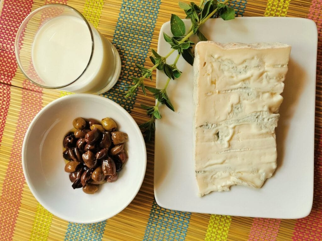 A piece of gorgonzola, some taggiasca olives, a glass of milk and twig marjoram.