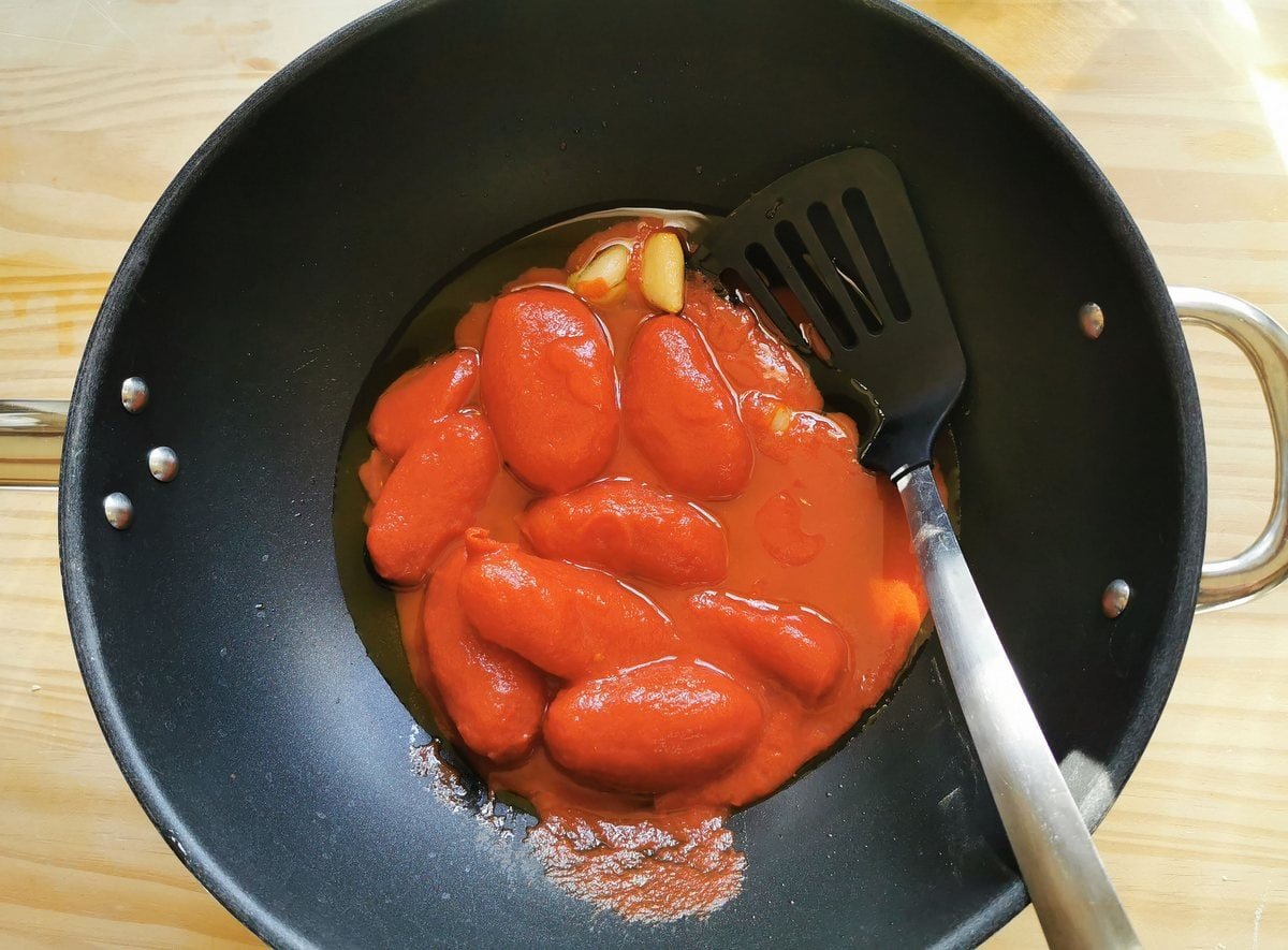 Hermeter peeled tomatoes in frying pan with garlic and olive oil.