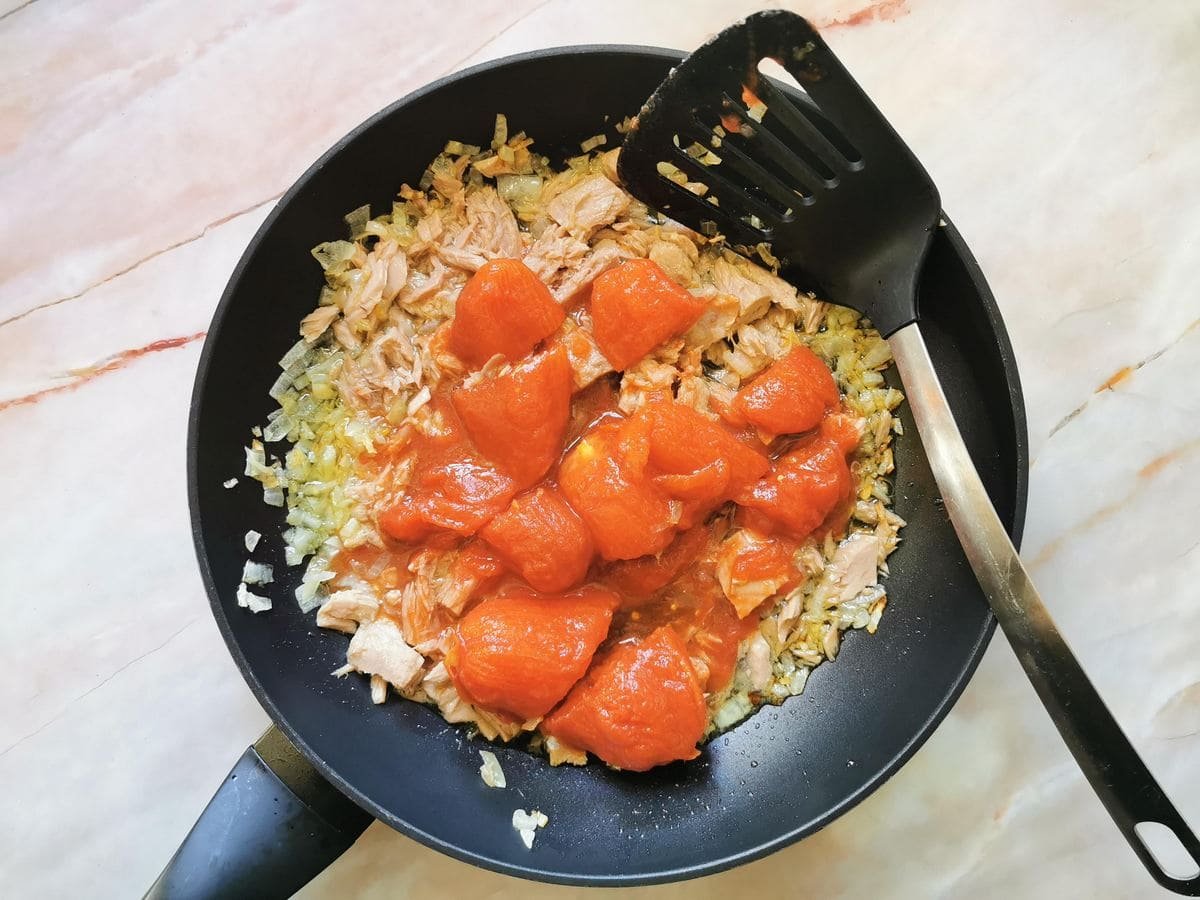 Hermetically peeled San Marzano tomatoes added onion and tuna in a large frying pan.