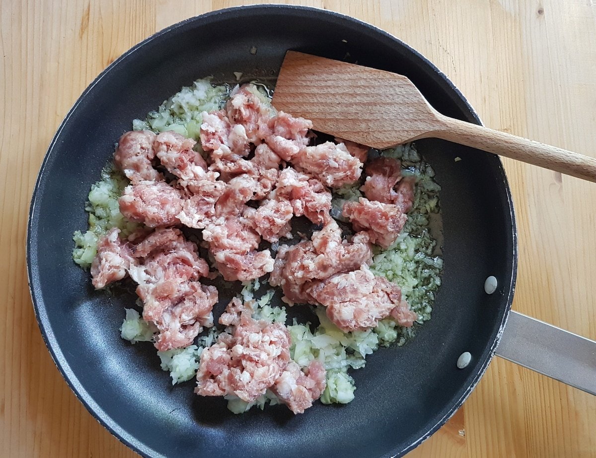 Crumbled sausage and chopped onion in a saucepan.