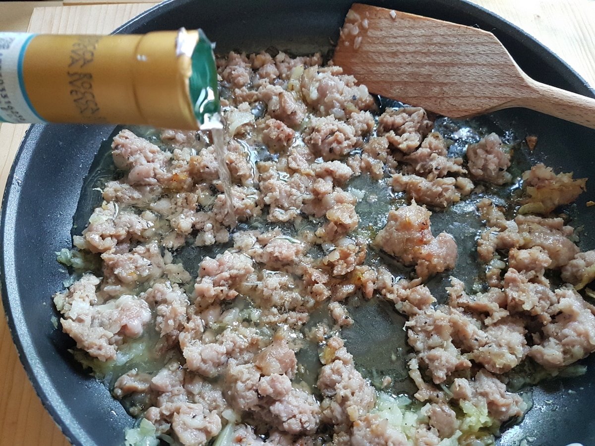 Crumbled sausage, chopped onion and white wine in a saucepan.