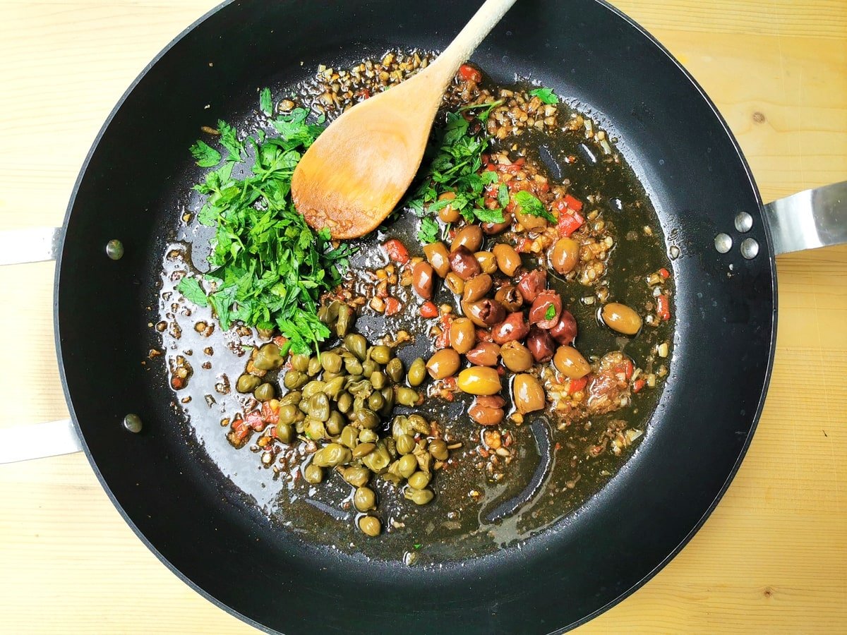 Chopped garlic, anchovy, peperoncino and parsley in frying pan with olives and capers.