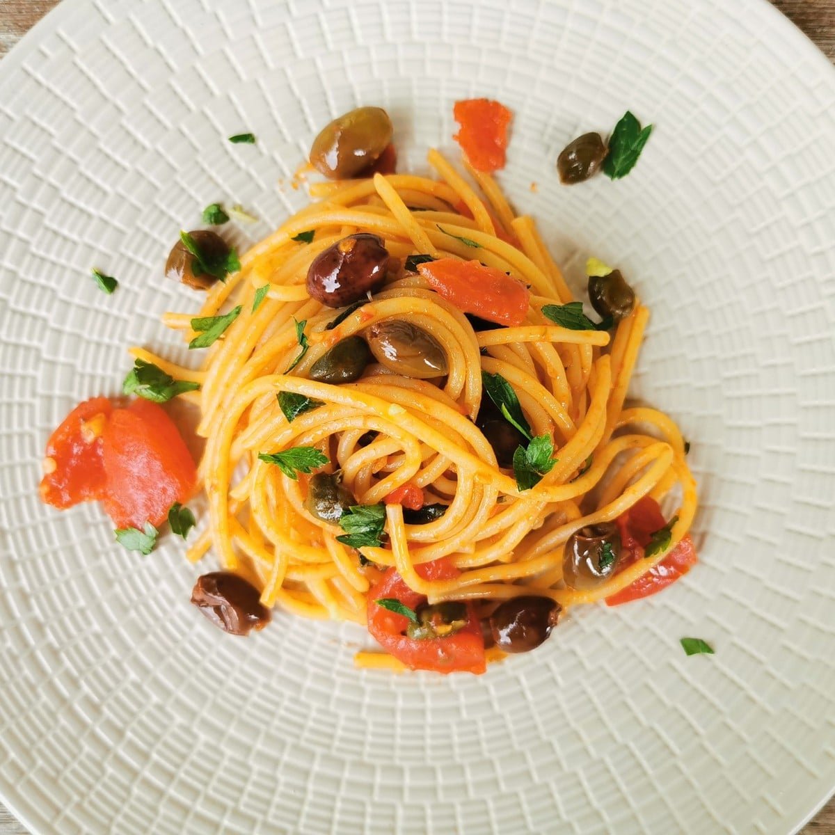 Pasta alla puttanesca decorated with flat leaf parsley.