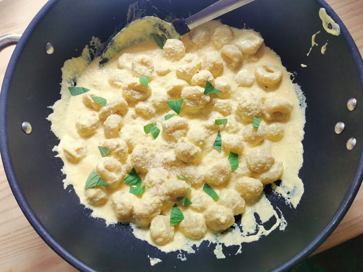 Potato gnocchi mixed with creamy saffron sauce in large saucepan.