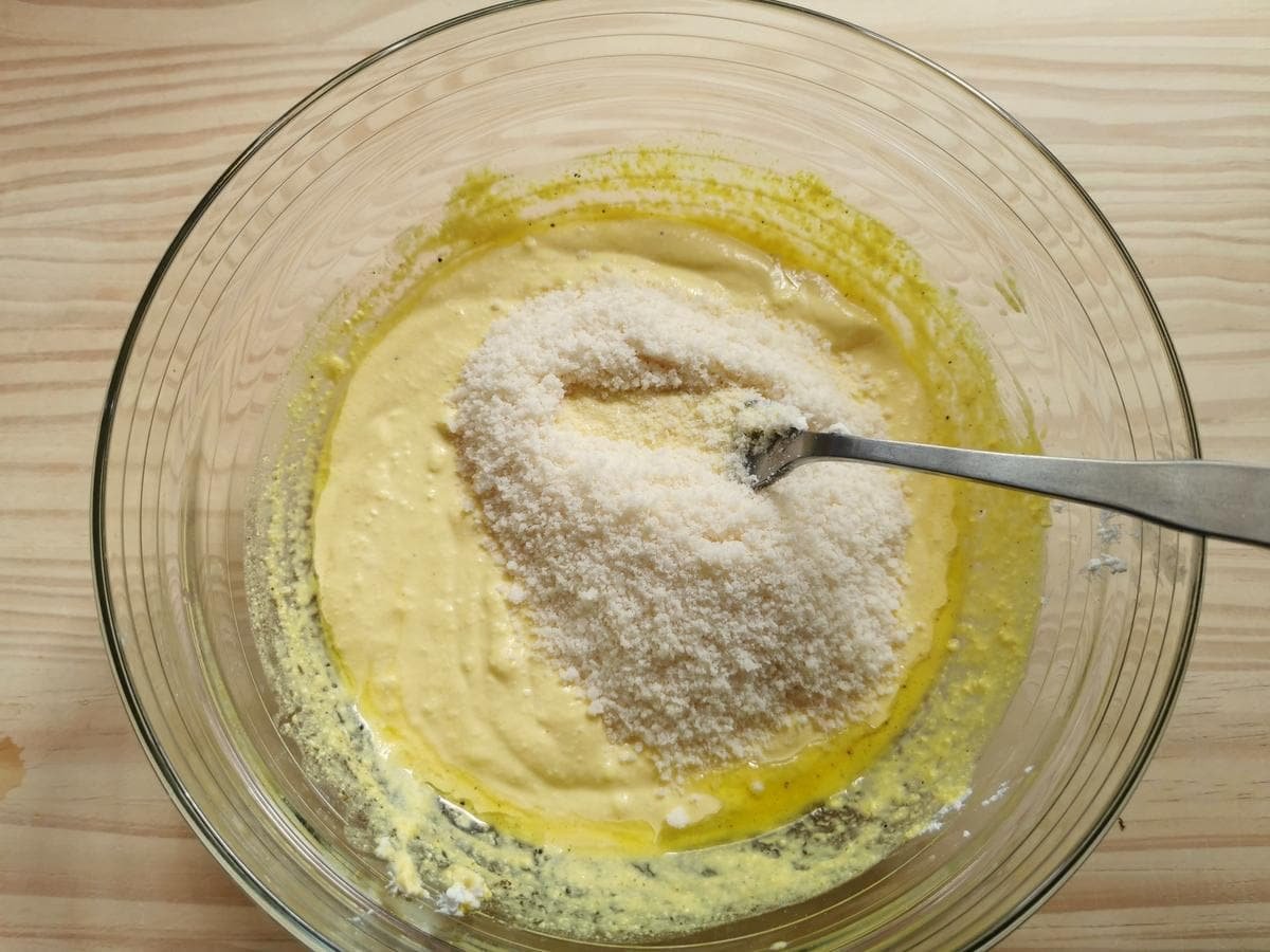 Sold Parmigiano added to saffron and ricotta cream sauce in glass bowl.